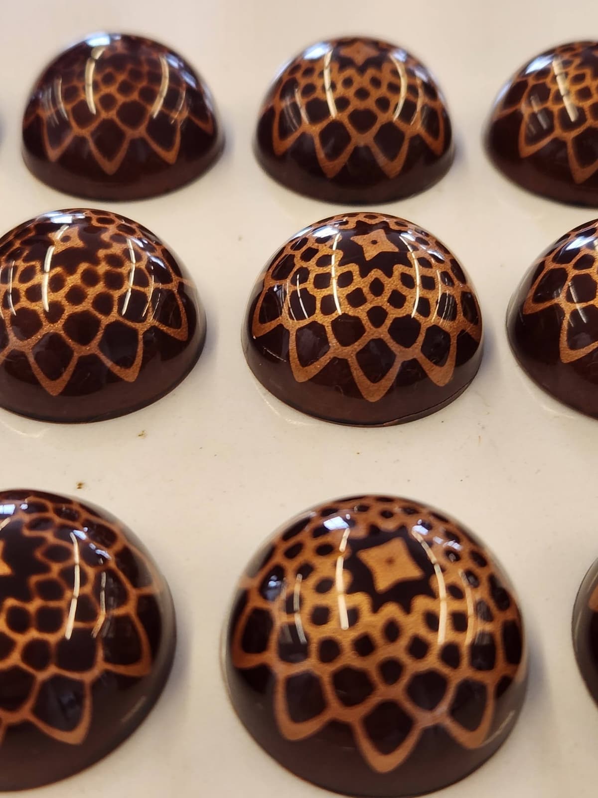 Glossy dark chocolate bonbons with hand-painted copper lace patterns